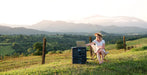 Person on grassy hillside using laptop powered by Bluetti AC180P Solar Power Station