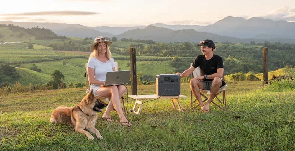 Two people and a dog enjoy the view with a Bluetti AC180P power station nearby